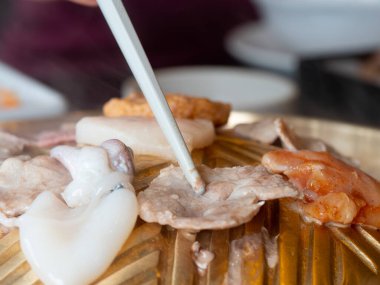 Domuz eti bir ızgarada kızartılır. Beyaz yemek çubukları kullanılarak. Sıcak ve dumanın tabaklardan yayıldığı yerde..