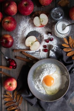 Tahta bir masada kırmızı elmalı bir kase un ve kırık yumurta.
