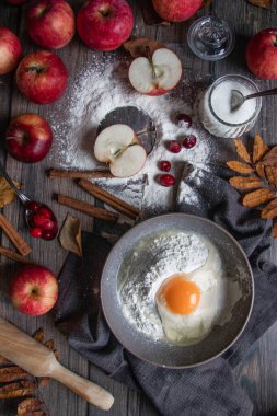 Tahta bir masada kırmızı elmalı bir kase un ve kırık yumurta.