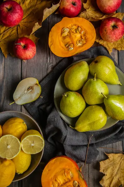Armutların, elmaların, balkabaklarının, limonların ve sarı yaprakların ahşap bir masa üzerindeki sonbaharı.