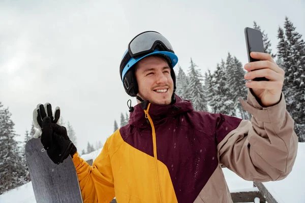 Desporto de inverno e recreação, lazer atividades ao ar livre. Homem de equipamento de esqui, com óculos de segurança, a fazer selfie. Homem de snowboarder caminhadas na montanha — Fotografia de Stock