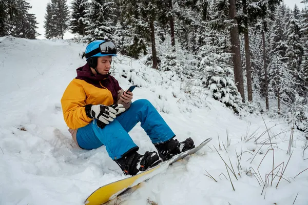 Aventura para o esporte de inverno. Homem de snowboarder caminhadas na montanha e mensagens de texto no telefone. À procura de pó para freeride — Fotografia de Stock