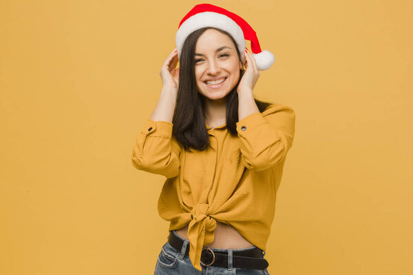 Photo of cute female in Christmas hat. Wears yellow shirt, isolated yellow color background