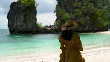 Sarı elbiseli ve şapkalı Asyalı kadın turist Hong Adası 'nda yürüyor, beyaz kumsal, Tayland, Krabi' de deniz..