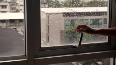 Kadın yağmurdan sonra pencereyi açıyor, evin çatısı şehrin arka planında.