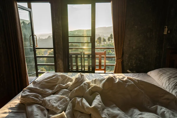 Bedroom with used blankets and pillows with green tea plantation view in the morning.