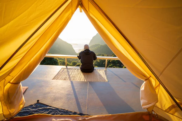 Asian male tourists sit on mats with warm morning light and beautiful mountains.