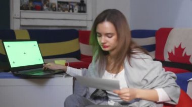 Finansal belgeleri elinde tutan genç bir kadın, internet bankacılığı için dizüstü bilgisayar kullanıyor, faturaları ödüyor dizüstü bilgisayarda çalışıyor, belgeleri işliyor, yeşil ekran üzerinde çalışıyor.