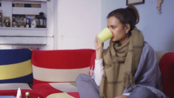 Вид сбоку молодая женщина чувствует себя нехорошо и измеряет температуру. Молодая женщина, сидящая на диване с шарфом, измеряет температуру.. — стоковое видео