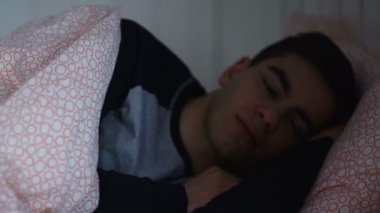 Genç bir adam yatakta uyuyor, gece telefonla bir mesaj alıyor..