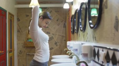 Genç bir kadının yan görünüşü, saçını at kuyruğu şeklinde topluyor. Güzel genç bir kadın aynanın önünde saçını tarıyor..