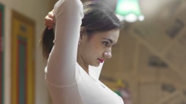 Genç bir kadının yan görünüşü, saçını at kuyruğu şeklinde topluyor. Güzel genç bir kadın aynanın önünde saçını tarıyor..