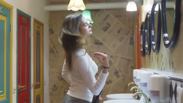 Вид сбоку на молодую женщину, одевающуюся перед зеркалом и расчесывающую волосы в отеле — стоковое видео