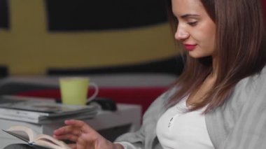 Genç bir kadın evinde bir sedirin üzerinde oturuyor ve kitap okuyor. Bir kadın boş zamanlarında rahat bir sedirin üzerinde dinleniyor. Hafta sonları iyi vakit geçir.