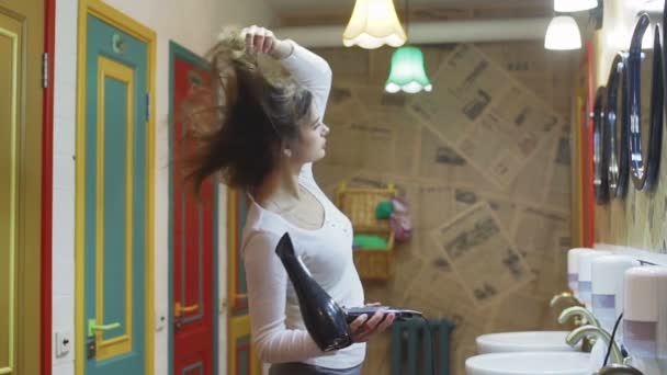 Genç bir kadın oteldeki saç kurutma makinesiyle saçını kurutuyor. — Stok video