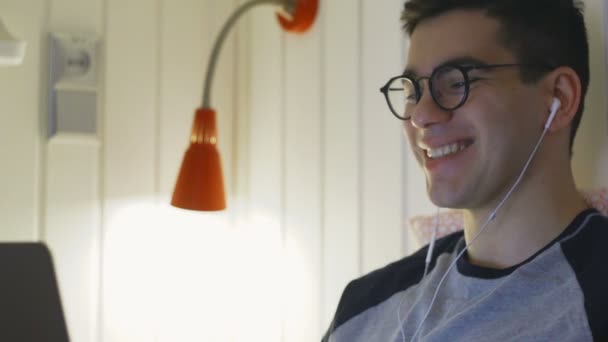 Joven sonriente, acostado en la cama y trabajando en un portátil, tecleando en el teclado, trabajando de noche, trabajo remoto desde casa por la noche. — Vídeos de Stock