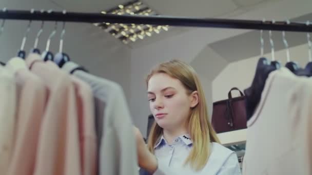 Una linda chica elige ropa en una tienda. Compras — Vídeos de Stock