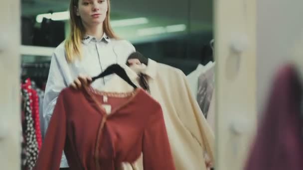 Kaunis tyttö kokeilee vaatteita vaatekaupan sovituskopissa. Ostokset — kuvapankkivideo