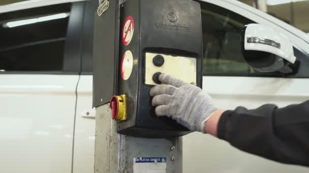 El mecánico del coche presiona un botón en el mecanismo de elevación y transporte del gato para bajar el coche. Reparación de automóviles, reparación, mantenimiento — Vídeos de Stock