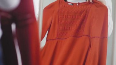 Genç bir kadın elbise deniyor ve ne giyeceğine karar veremiyor, kızıyor ve elbiselerini yere atıyor. Tanımlanamayan bir kızın yakın çekimi.