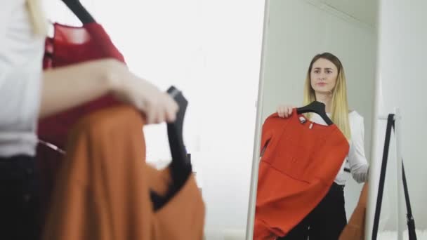 En ung kvinde forsøger på tøj og kan ikke beslutte, hvad de skal bære, bliver vred og kaster sit tøj på gulvet. – Stock-video