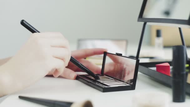 Una paleta con sombra de ojos y un cepillo de maquillaje. Un primer plano de una mujer compone una paleta de cosméticos con diferentes colores. — Vídeos de Stock