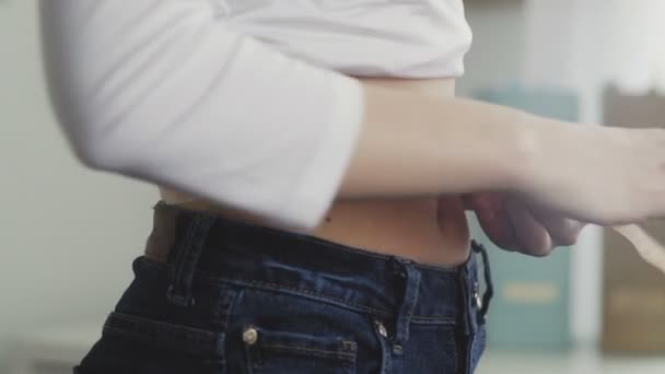 Uma jovem mulher fica na frente de um espelho e mede a circunferência da cintura com uma fita métrica. Close-up — Vídeo de Stock