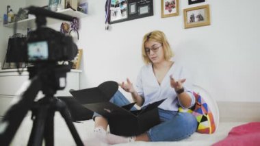 Gözlüklü genç bir kadın gülümsüyor ve kameraya yeni bir alımdan bahsediyor. Kutu açılıyor