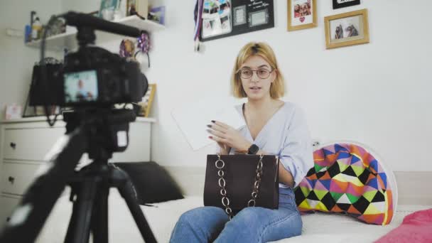 Een jonge vrouw met een bril glimlacht en vertelt de camera over een nieuwe aankoop. Unboxing — Stockvideo