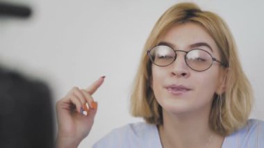 Kanepede oturan, gülümseyen ve kamerayla konuşan gözlüklü genç bir kadının yakın çekimi. Abonelerine veda ediyor.
