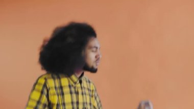 Turuncu arka planda Afrikalı saç stili olan genç bir adam dans ediyor. Renkli bir arkaplanda dans etmek.