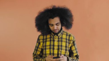 Turuncu arka planda Afrikalı saç stili olan genç bir adam telefonuna konuşuyor..