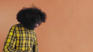 Turuncu arka planda Afrikalı saç stili olan genç bir adam telefonunu çıkardı, mesaja baktı ve cebine geri koydu. Renkli bir arkaplanda duygular