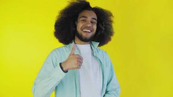 Un hombre afroamericano feliz mirando a la cámara, muestra un parecido con su mano, se encuentra aislado sobre un fondo amarillo — Vídeos de Stock