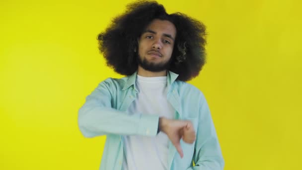 An African-American man looks at the camera, gives a thumbs down, stands isolated on a yellow background — Stock Video