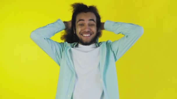 Młody człowiek z afro fryzurą na żółtym tle jest szczęśliwy. Emocje na kolorowym tle. — Wideo stockowe