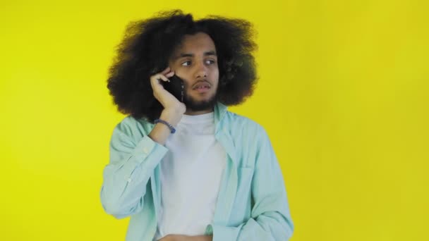 Un giovane con un'acconciatura africana su sfondo giallo sta parlando al telefono. Su uno sfondo colorato — Video Stock