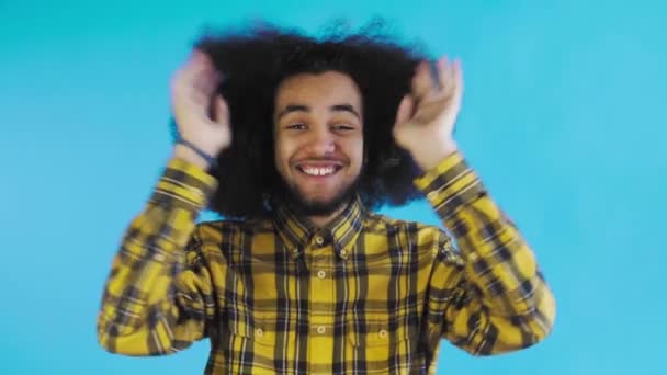 Un jeune homme avec une coiffure africaine sur fond bleu est heureux. Émotions sur un fond coloré. — Video