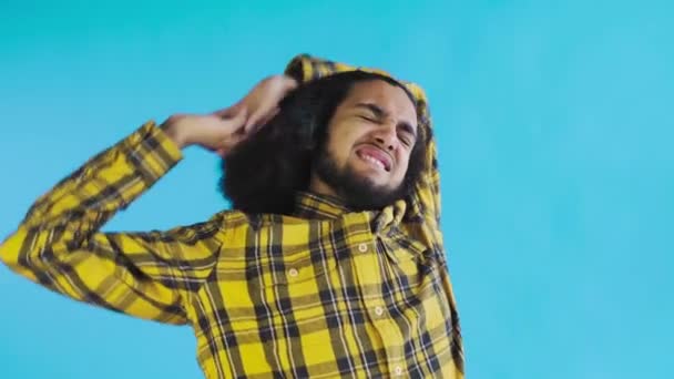 Un joven con un peinado africano sobre un fondo azul está cansado. Emociones sobre un fondo coloreado. — Vídeo de stock