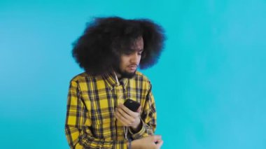 Mavi arka planda Afrikalı saç stili olan genç bir adam müzik ve kulaklık dinliyor. Renkli bir arkaplanda