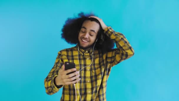 Um jovem com um penteado africano em um fundo azul em fones de ouvido se comunica via link de vídeo. Em um fundo colorido — Vídeo de Stock