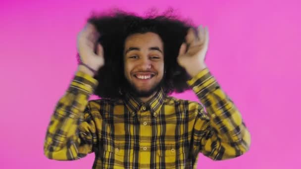 Un jeune homme avec une coiffure africaine sur fond rose est heureux. Émotions sur un fond coloré. — Video