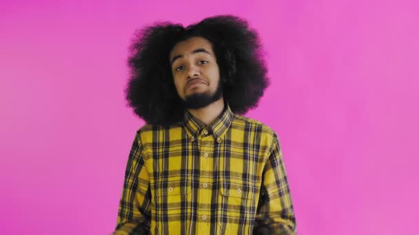 Um jovem com um penteado africano em um fundo rosa encolhe os ombros. Emoções em um fundo colorido. — Vídeo de Stock