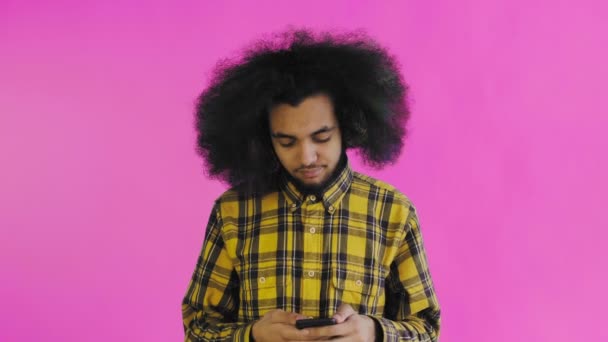 Молодой человек с африканской прической на розовом фоне разговаривает в свой телефон. — стоковое видео