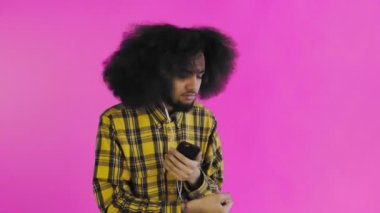Pembe arka planda Afrikalı saç stili olan genç bir adam müzik ve kulaklık dinliyor. Renkli bir arkaplanda