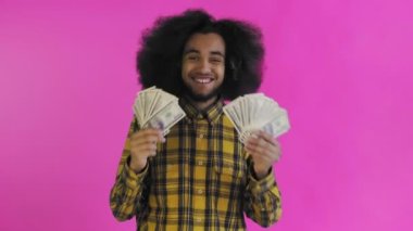 Elinde banknot yelpazesi olan mutlu bir Afro-Amerikalı adam pembe bir arka planda tek başına kameraya bakıyor.