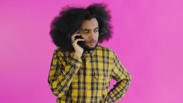 一个有着粉色背景的非洲发型的年轻人正在电话里交谈。在彩色背景上 — 图库视频影像
