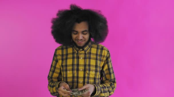 Szczęśliwy Afroamerykanin trzymający banknoty w rękach, liczący je i patrzący w kamerę, stojący samotnie na różowym tle — Wideo stockowe