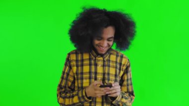 Yeşil arka planda Afrikalı saç stili olan genç bir adam telefona bakar ve biriyle mutlu mesut mesajlaşır. Renkli bir arkaplanda duygular