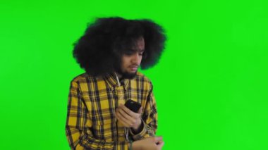 Yeşil arka planda Afrikalı saç stili olan genç bir adam müzik ve kulaklık dinliyor. Renkli bir arkaplanda